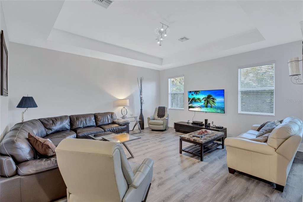 A living room features a large sectional, two armchairs, a television, and light wood flooring — 9019 HERITAGE SOUND DRIVE, BRADENTON, FL