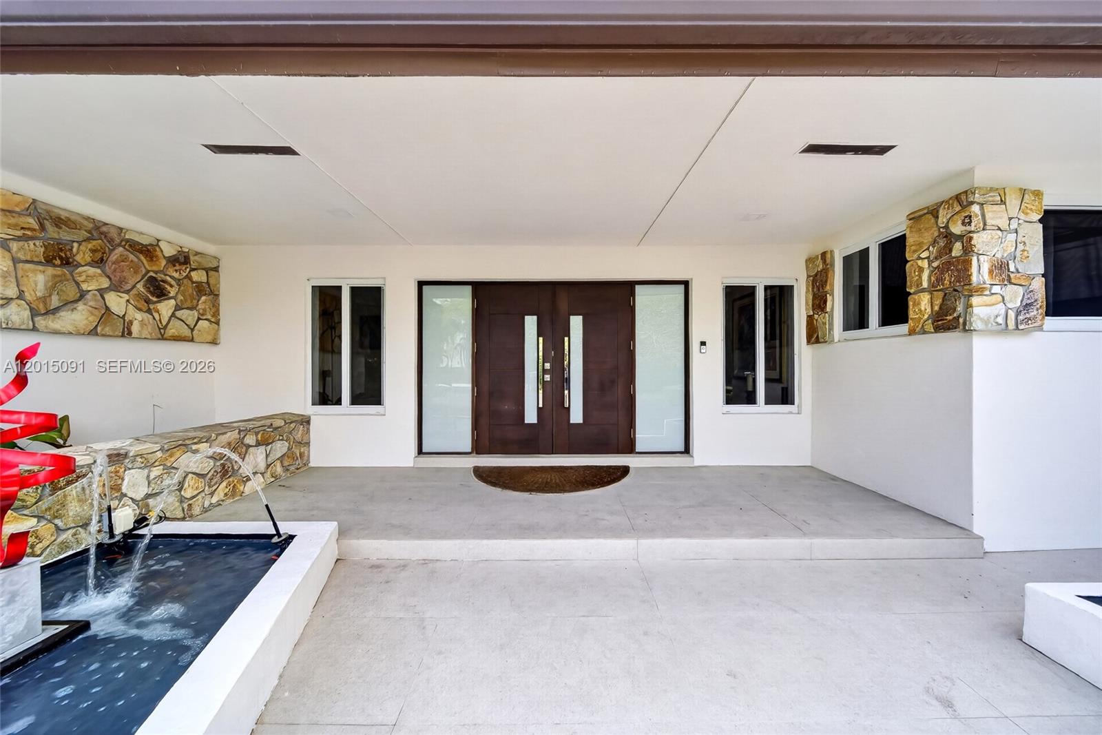A modern home entrance features a double door, a stone-accented wall, and a water fountain — 6650 SW 112th St, Pinecrest FL 33156, PINECREST, FL
