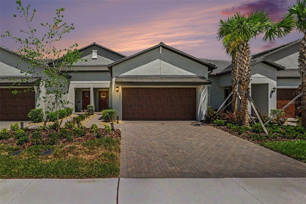 A single-story house with a two-car garage and a paved driveway under a sunset sky — 10911 RUSTIC EVE COURT, LAND O LAKES, FL