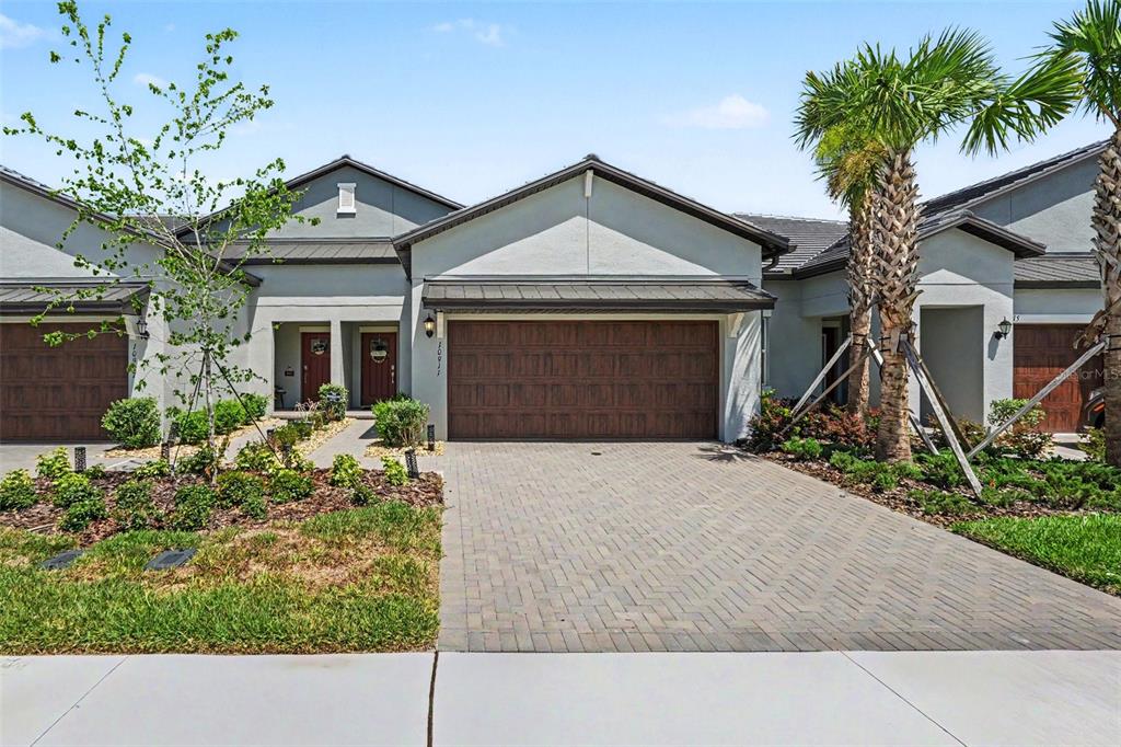 A single-story townhouse with a paved driveway, a two-car garage, and a palm tree — 10911 RUSTIC EVE COURT, LAND O LAKES, FL