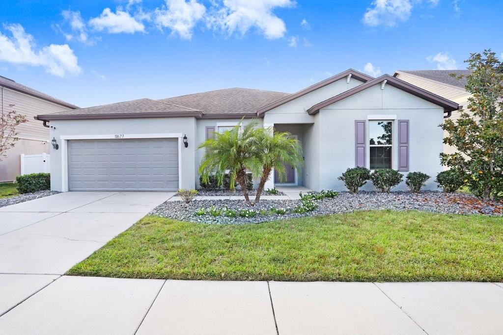 A single-story suburban house with a gray stucco exterior, a two-car garage, and a palm tree — 11677 BRIGHTON KNOLL LOOP, RIVERVIEW, FL