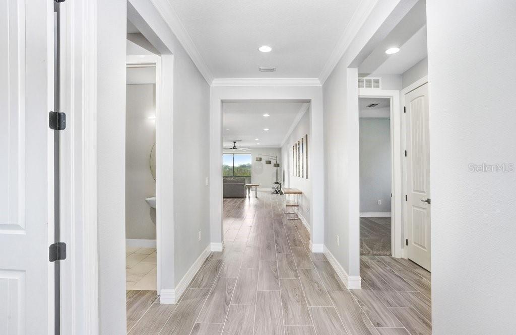 A hallway with light wood-look tile flooring leads to an open-concept living area — 11677 BRIGHTON KNOLL LOOP, RIVERVIEW, FL
