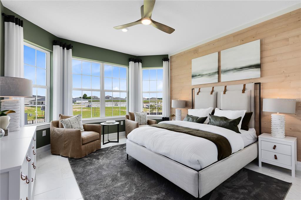 A bedroom features a wood-paneled accent wall, a bed, two armchairs, and large bay windows — 5237 HANDSOME HILLS DRIVE, MOUNT DORA, FL