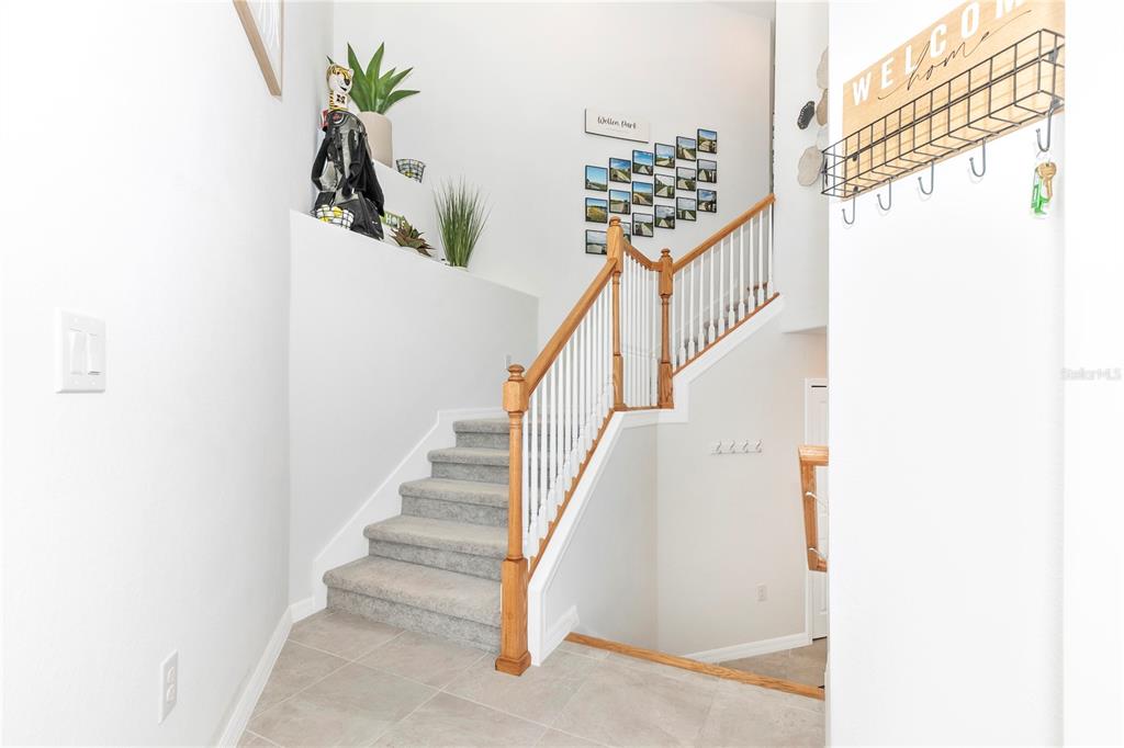 An interior view of a foyer featuring a carpeted staircase with wooden railings and tile flooring — 17560 BORACAY COURT UNIT 202, VENICE, FL