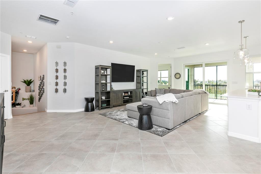 A living room features gray tile flooring, a sectional sofa, and a wall-mounted television — 17560 BORACAY COURT UNIT 202, VENICE, FL