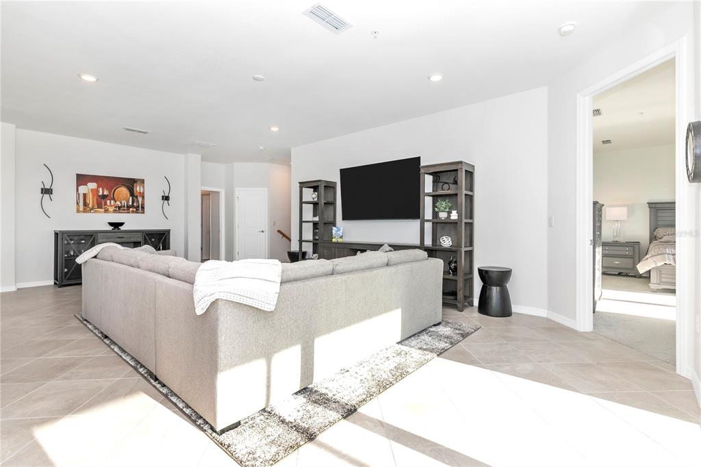 A living room features a large gray sectional sofa, a wall-mounted television, and tile flooring — 17560 BORACAY COURT UNIT 202, VENICE, FL