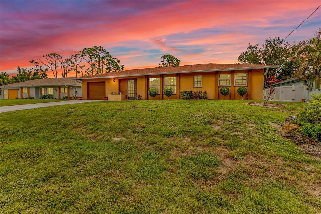 A single-story house with a yellow exterior and a garage under a vibrant sunset sky — 2626 AUBURN BOULEVARD, PORT CHARLOTTE, FL