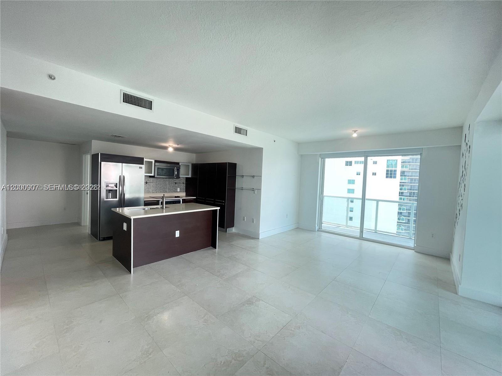 An open-concept kitchen with dark cabinetry and a central island overlooks a spacious living area — 1900 N Bayshore Dr # 3311, Miami FL 33132, MIAMI, FL