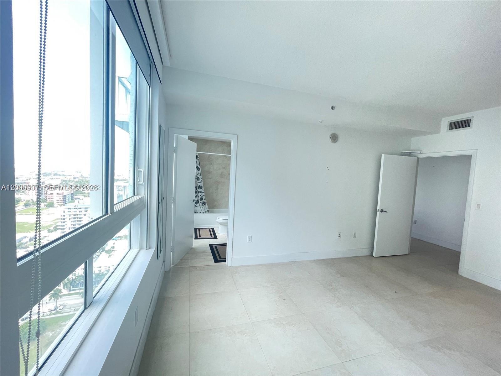 A bright room with large windows, tile flooring, and doorways leading to a bathroom and hallway — 1900 N Bayshore Dr # 3311, Miami FL 33132, MIAMI, FL
