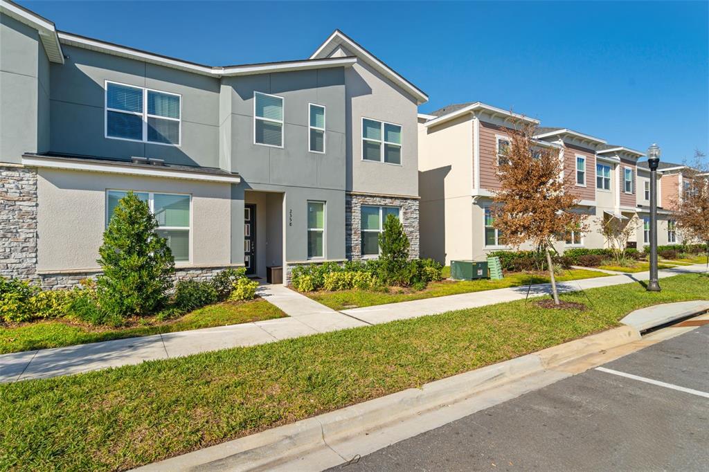 A two-story townhouse exterior features gray siding, stone accents, and a concrete walkway — 2358 ZABALLINA PLACE, KISSIMMEE, FL