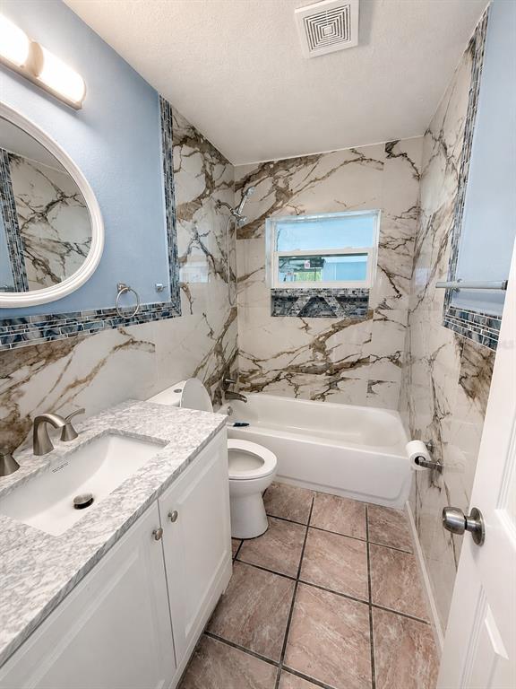 A bathroom features a white vanity, a toilet, and a tub with marble-patterned tile walls — 4824 LIMESTONE DRIVE, PORT RICHEY, FL