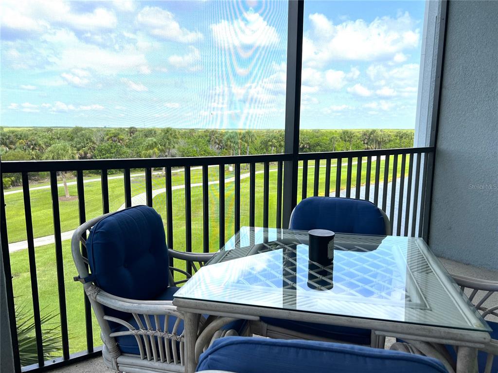 A screened-in balcony features a glass-topped table, blue chairs, and a view of greenery — 14091 HERITAGE LANDING BOULEVARD UNIT 133, PUNTA GORDA, FL