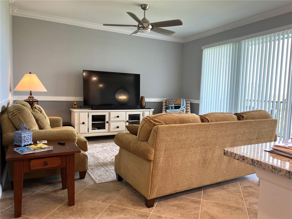A living room features tan sofas, a white media console, and a ceiling fan — 14091 HERITAGE LANDING BOULEVARD UNIT 133, PUNTA GORDA, FL