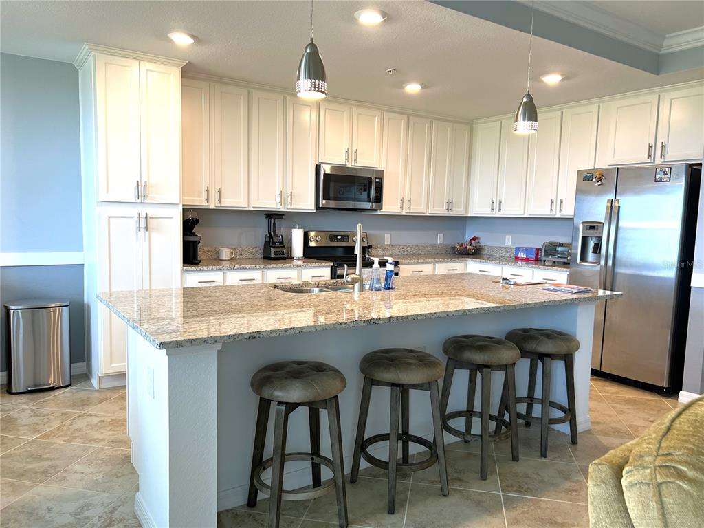 A kitchen features white cabinets, granite countertops, a large island with stools, and stainless appliances — 14091 HERITAGE LANDING BOULEVARD UNIT 133, PUNTA GORDA, FL