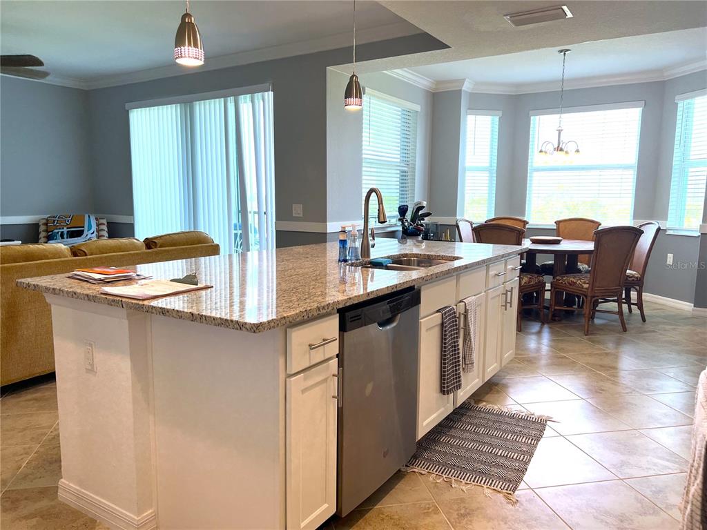 A kitchen island with granite countertops and a stainless steel dishwasher faces a dining area — 14091 HERITAGE LANDING BOULEVARD UNIT 133, PUNTA GORDA, FL
