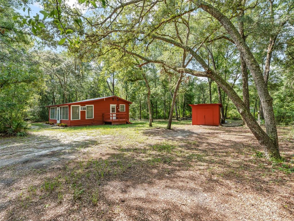 A red cabin and a matching storage shed sit on a wooded lot — 4935 SW 124TH LN, WEBSTER, FL