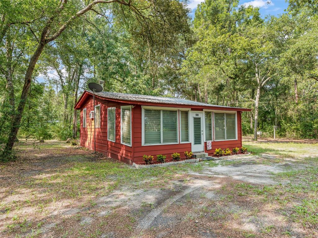 A small, red-sided house with a metal roof sits in a wooded, grassy lot — 4935 SW 124TH LN, WEBSTER, FL