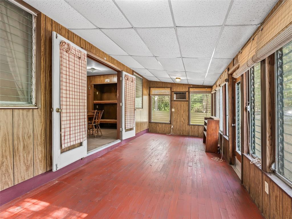 A sunroom features wood-paneled walls, a painted red floor, and a drop ceiling — 4935 SW 124TH LN, WEBSTER, FL