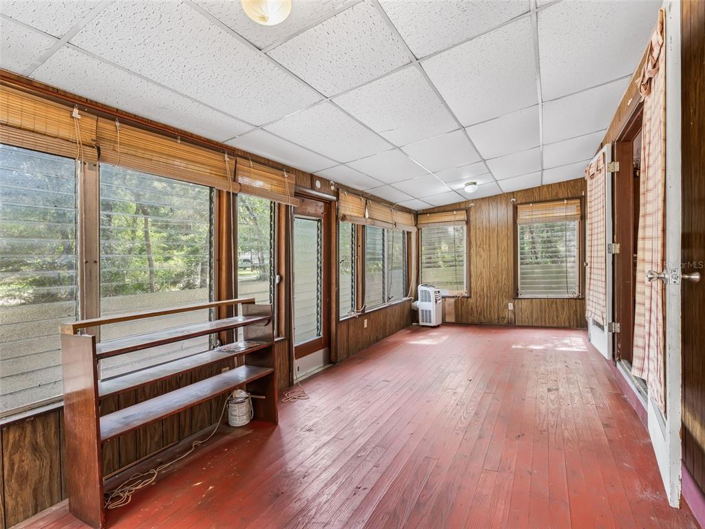 A sunroom with wood-paneled walls, jalousie windows, a drop ceiling, and red-painted wooden flooring — 4935 SW 124TH LN, WEBSTER, FL