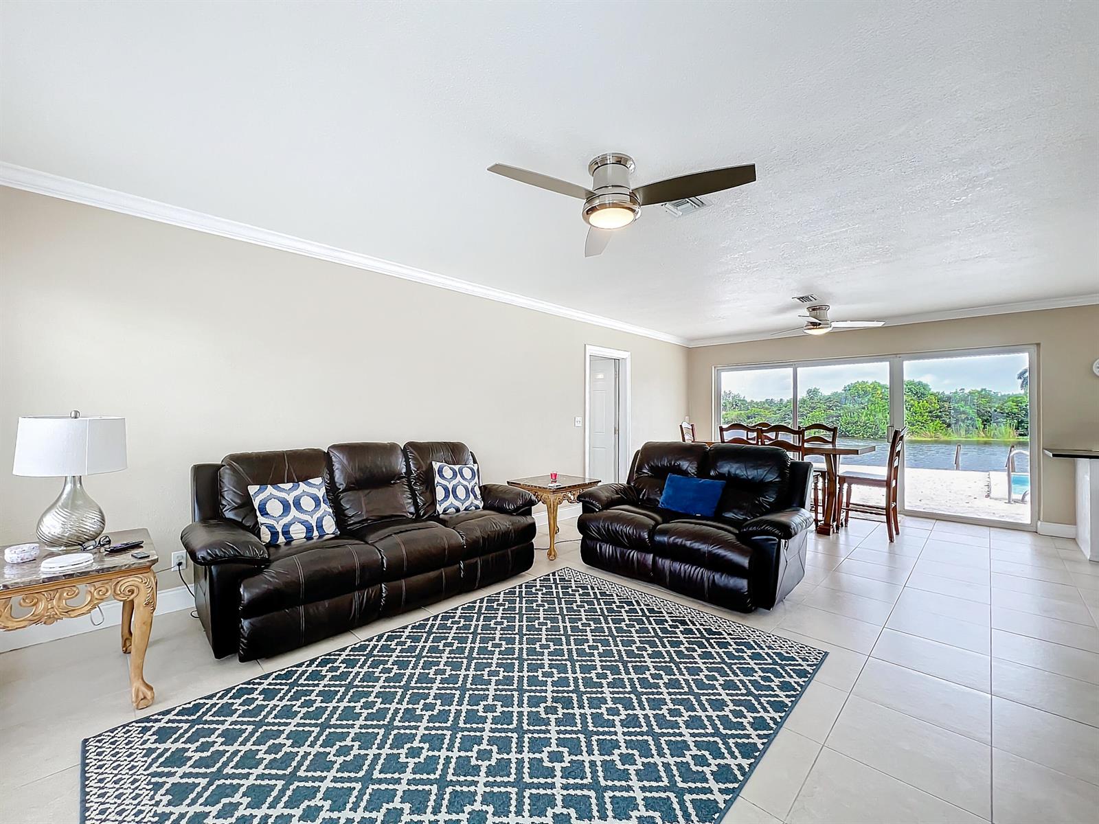 A living room with dark leather sofas, a patterned rug, and a view of water — 6803 Kingston Drive, Lake Worth FL 33462, LAKE WORTH, FL