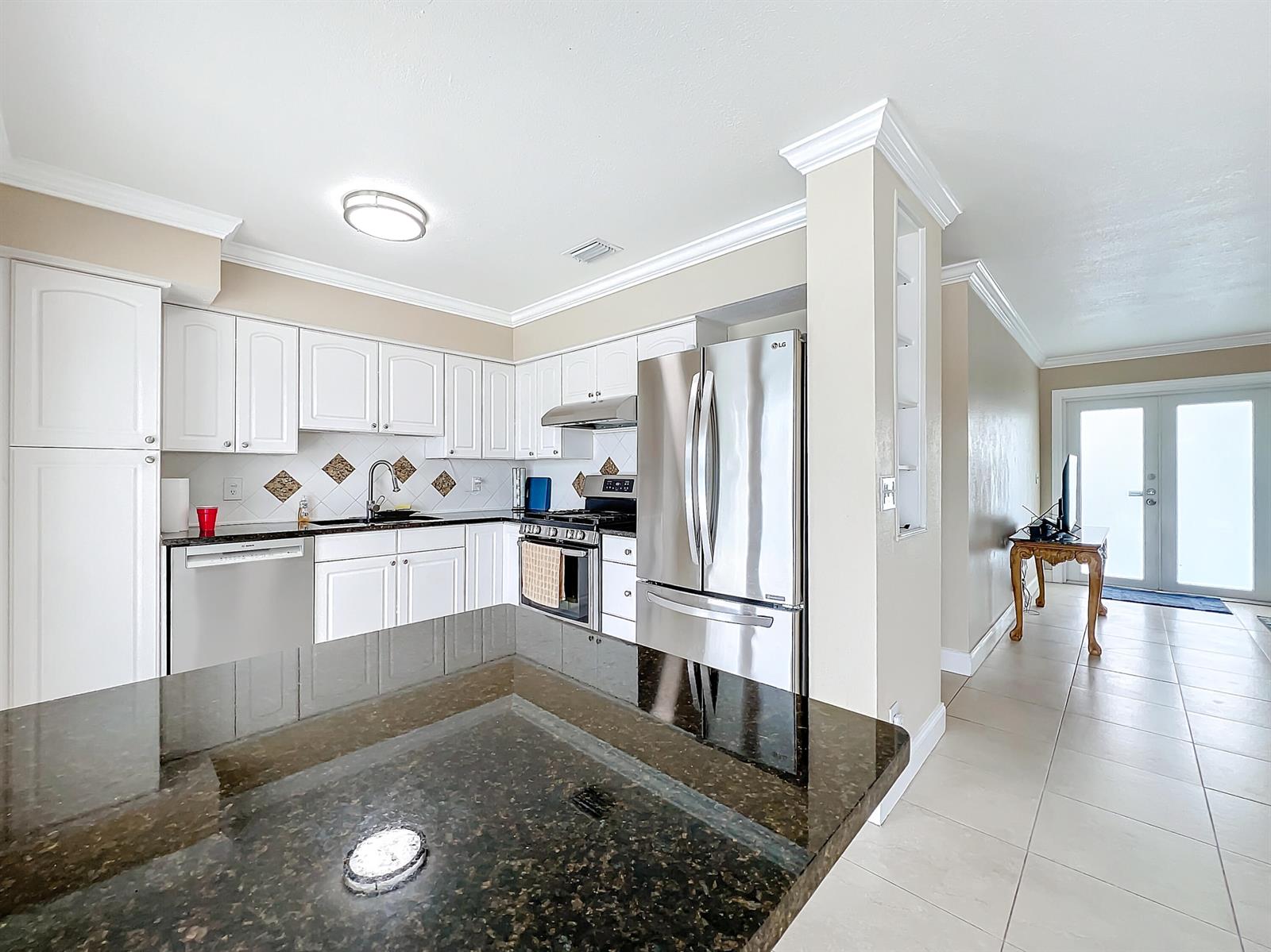 A kitchen features white cabinets, dark granite countertops, stainless steel appliances, and tile flooring — 6803 Kingston Drive, Lake Worth FL 33462, LAKE WORTH, FL