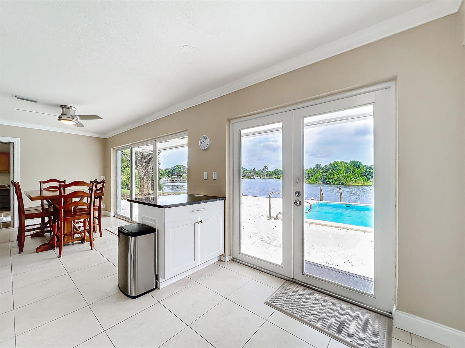A dining area and kitchen island overlook a swimming pool and a waterfront view — 6803 Kingston Drive, Lake Worth FL 33462, LAKE WORTH, FL