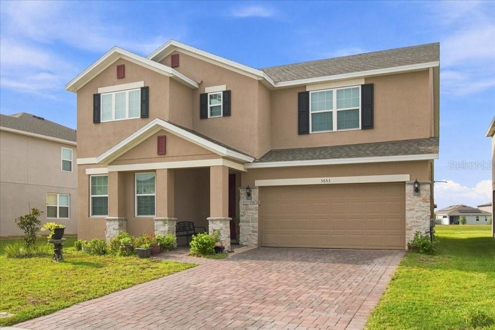 A two-story suburban house with a tan stucco exterior, stone accents, and a paved driveway — 5653 CAMILLA STREET, ST CLOUD, FL