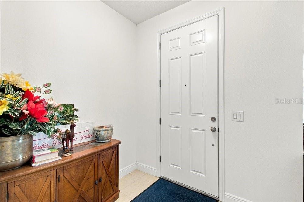 A white front door opens into a foyer with a wooden cabinet and floral arrangement — 5653 CAMILLA STREET, ST CLOUD, FL