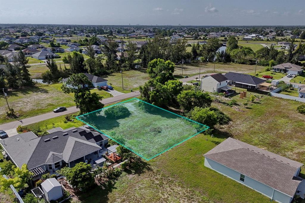 An aerial view shows a vacant, rectangular residential lot outlined in blue between two houses — 3912 NE 9TH AVENUE, CAPE CORAL, FL