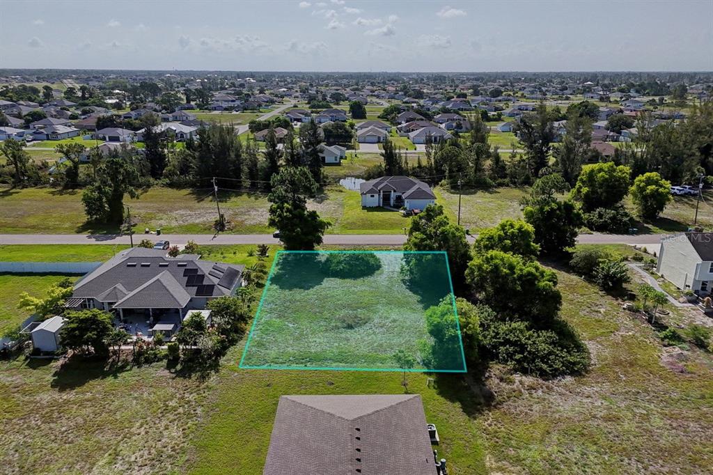 An aerial view shows a vacant residential lot outlined in blue between two houses — 3912 NE 9TH AVENUE, CAPE CORAL, FL