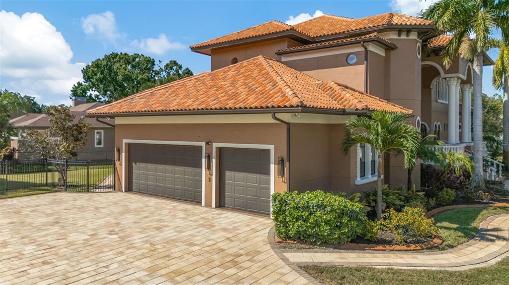 A tan two-story house features a three-car garage, a terracotta tile roof, and a paver driveway — 1079 ASHLAND AVENUE, TARPON SPRINGS, FL