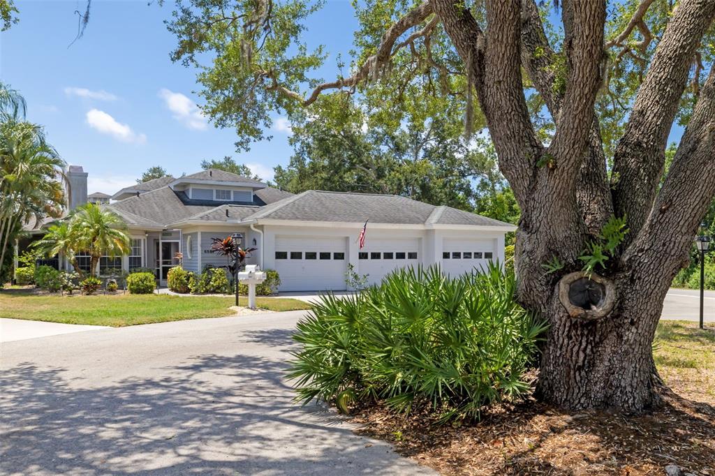 A single-story house with a three-car garage and a large tree in the front yard — 6581 APPROACH ROAD UNIT 63, SARASOTA, FL
