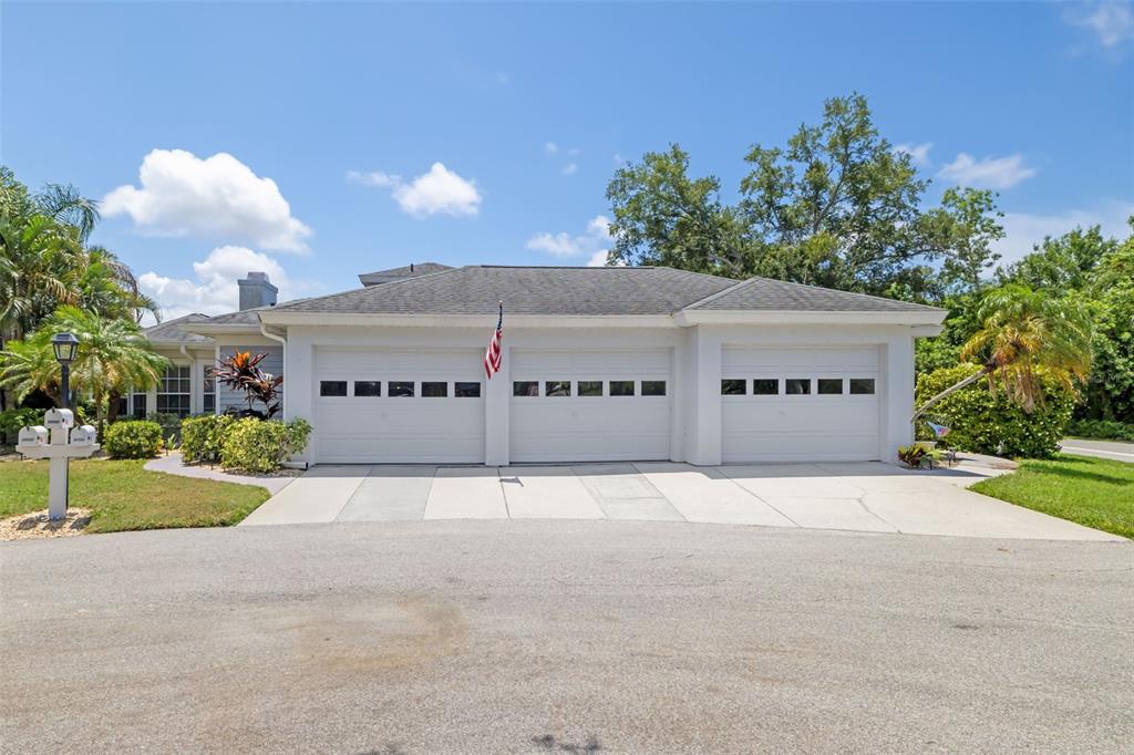 A three-car garage with white doors and an American flag sits under a hip roof — 6581 APPROACH ROAD UNIT 63, SARASOTA, FL