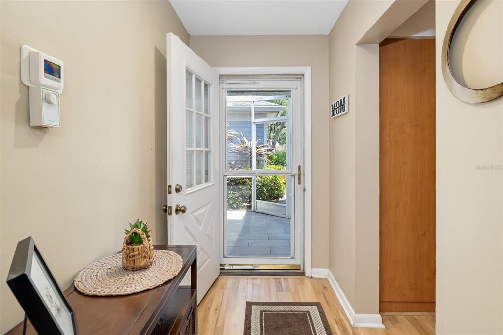 An entryway features a white door, light wood flooring, and a view of a screened porch — 6581 APPROACH ROAD UNIT 63, SARASOTA, FL
