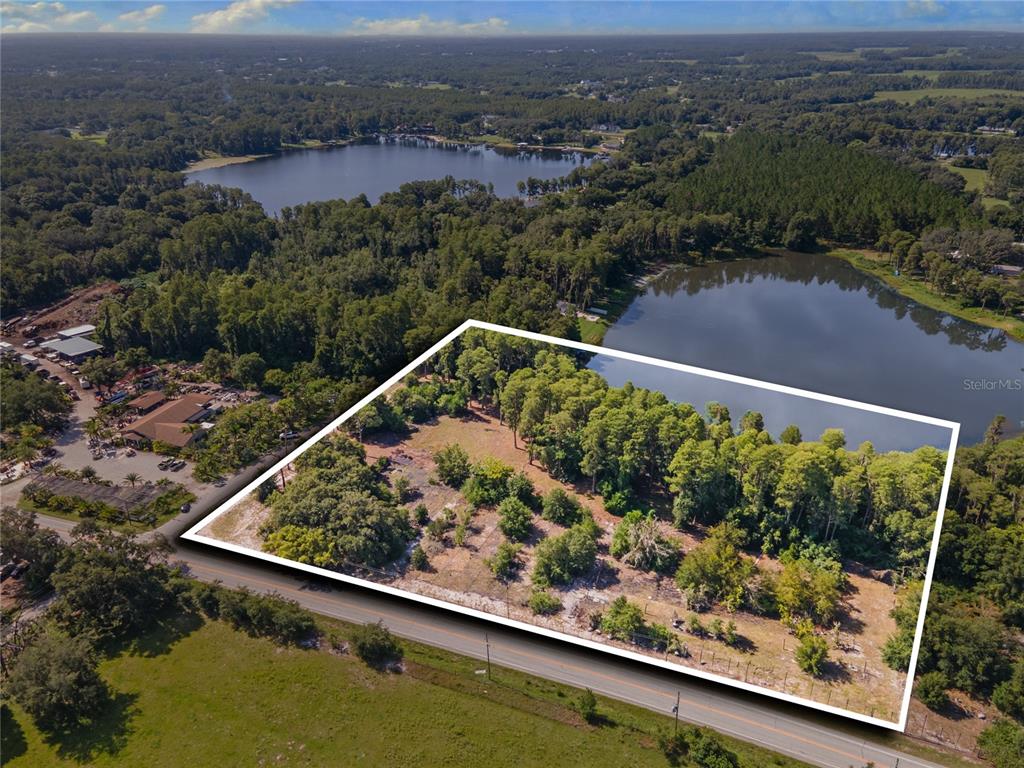 An aerial view shows a vacant, partially wooded lot outlined in white next to a lake — 18150 BURRELL ROAD, ODESSA, FL