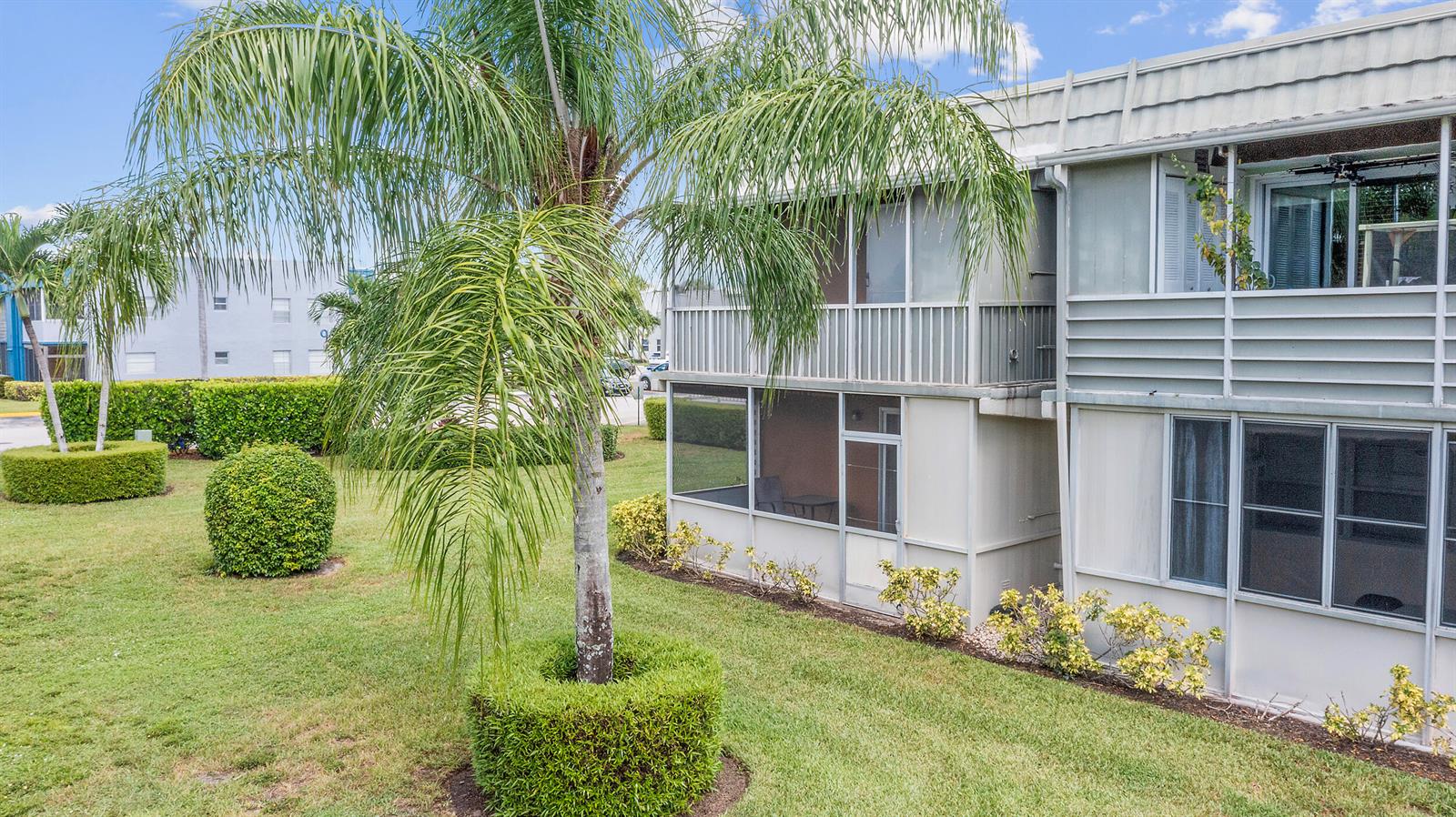 The exterior of a two-story apartment building features screened balconies and manicured landscaping — 723 Flanders P, Delray Beach FL 33484, DELRAY BEACH, FL