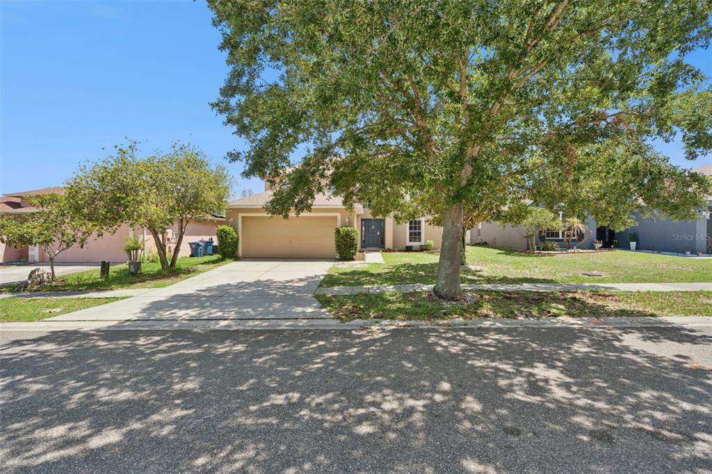 A two-story suburban house with a tan exterior, a two-car garage, and a large tree — 416 BARLYN AVENUE, HAINES CITY, FL