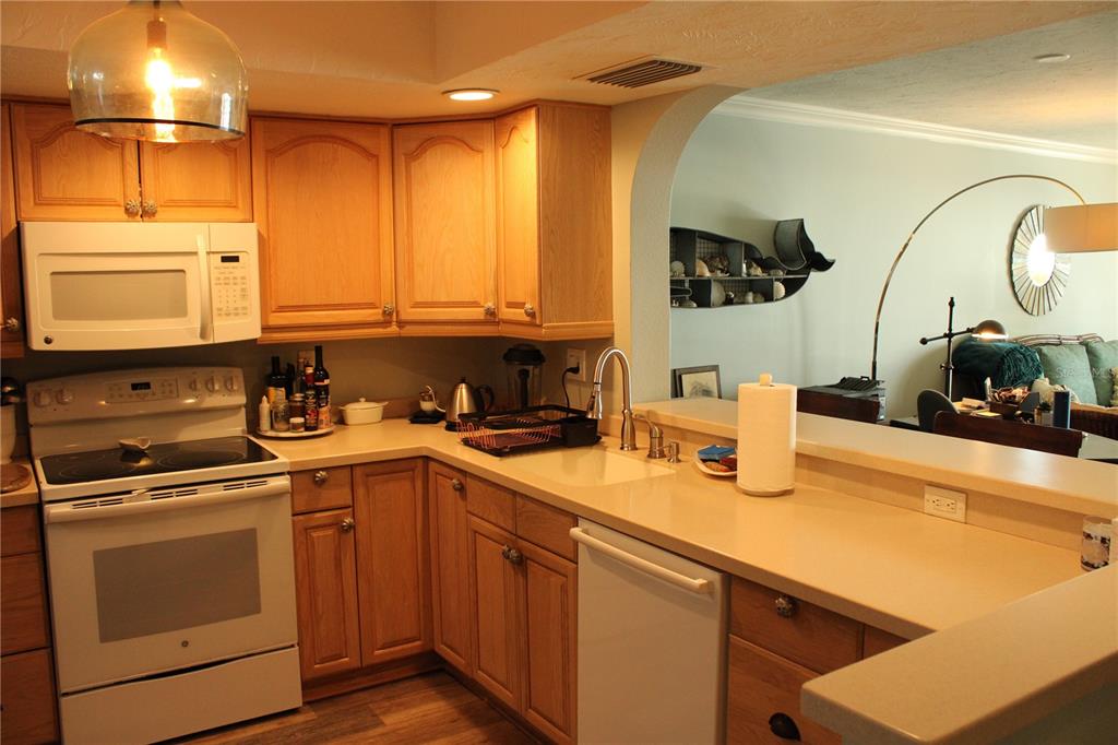 A kitchen with light wood cabinets, white appliances, and a peninsula overlooking a living area — 6470 MOURNING DOVE DRIVE UNIT 203, BRADENTON, FL