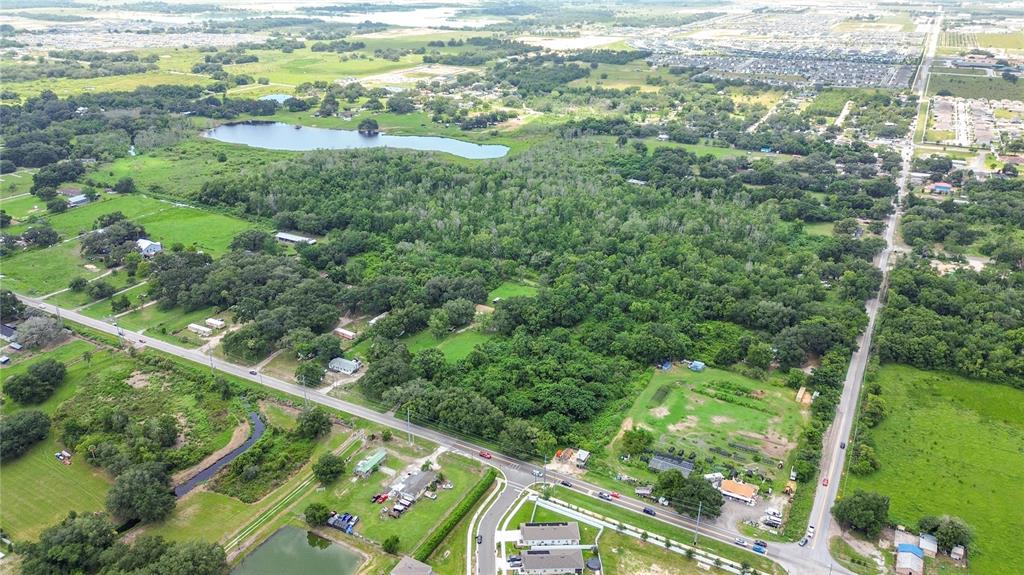 An aerial view shows a large wooded area surrounded by residential properties, roads, and ponds — JOHNSON AVENUE E, HAINES CITY, FL