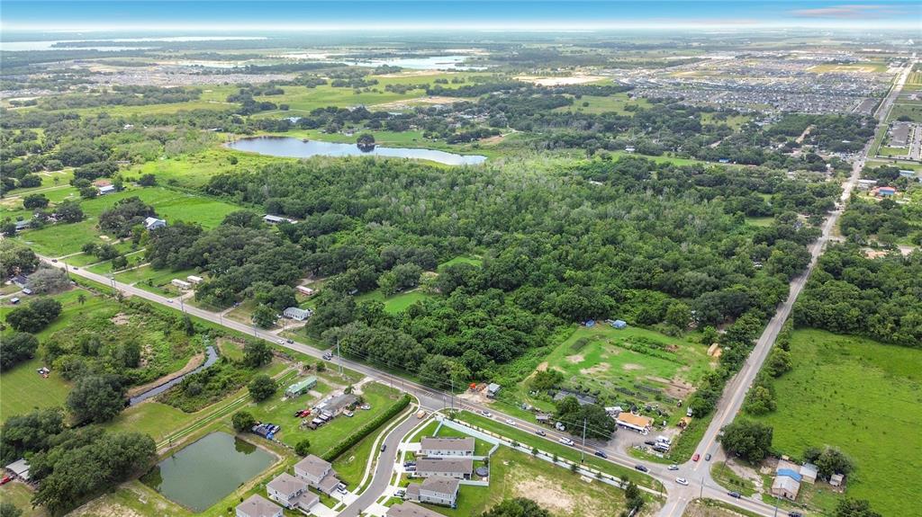 An aerial view shows a large wooded lot bordered by roads, houses, and a pond — JOHNSON AVENUE E, HAINES CITY, FL