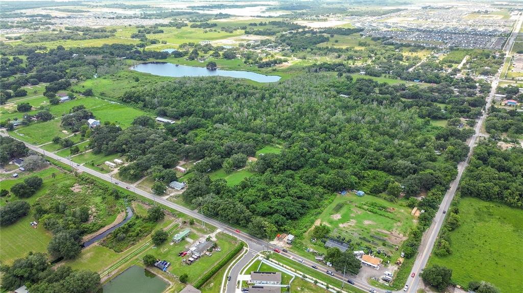 An aerial view shows a large wooded area surrounded by roads, fields, and residential properties — JOHNSON AVENUE E, HAINES CITY, FL