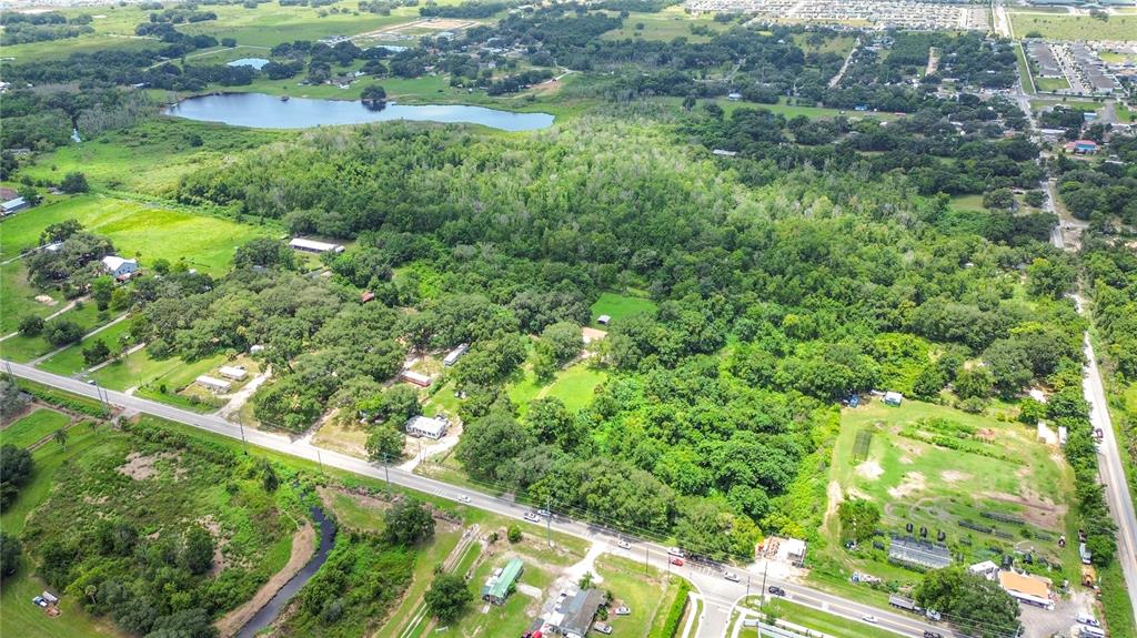 An aerial view shows a large, wooded property with scattered buildings and a nearby lake — JOHNSON AVENUE E, HAINES CITY, FL