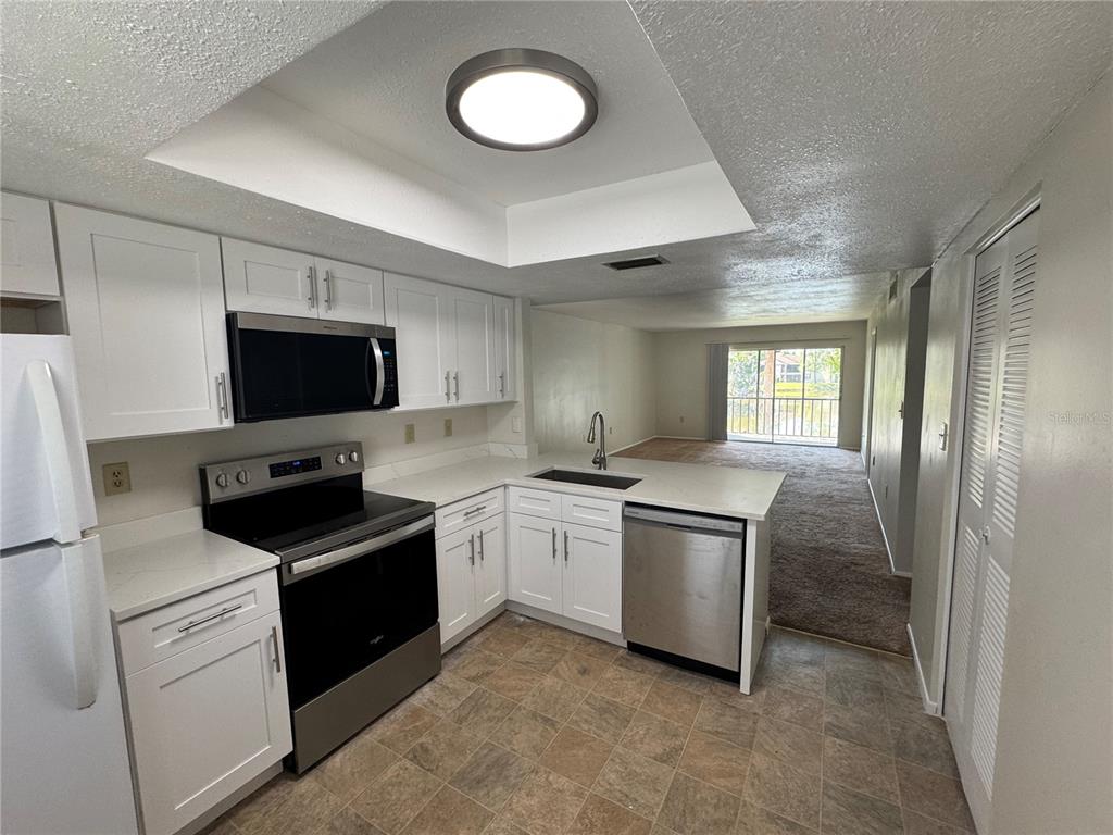 A kitchen with white cabinets, stainless steel appliances, and a view into the living area — 212 CYPRESS LANE, OLDSMAR, FL