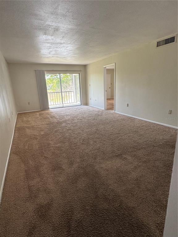 An empty living room with beige carpet, light-colored walls, and a sliding glass balcony door — 212 CYPRESS LANE, OLDSMAR, FL