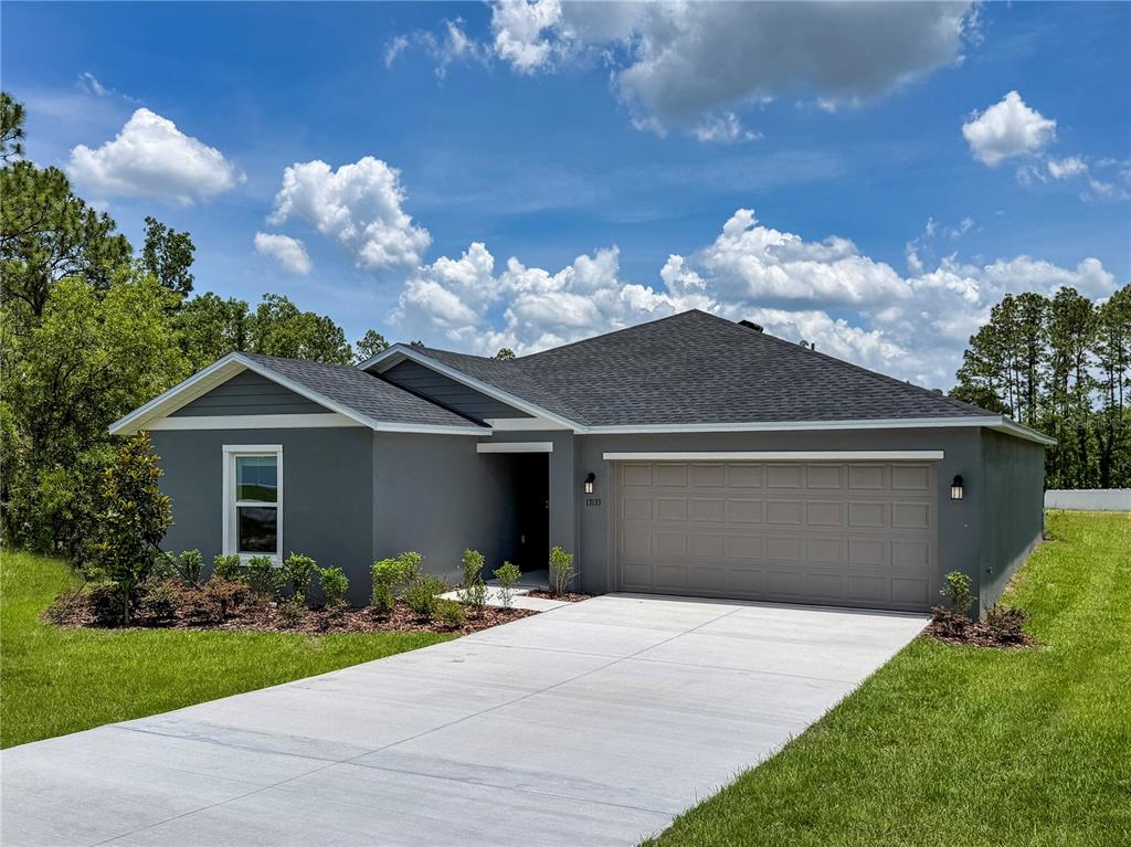 A gray single-story house with a two-car garage and a concrete driveway under a blue sky — 13079 SW 86TH COURT, OCALA, FL