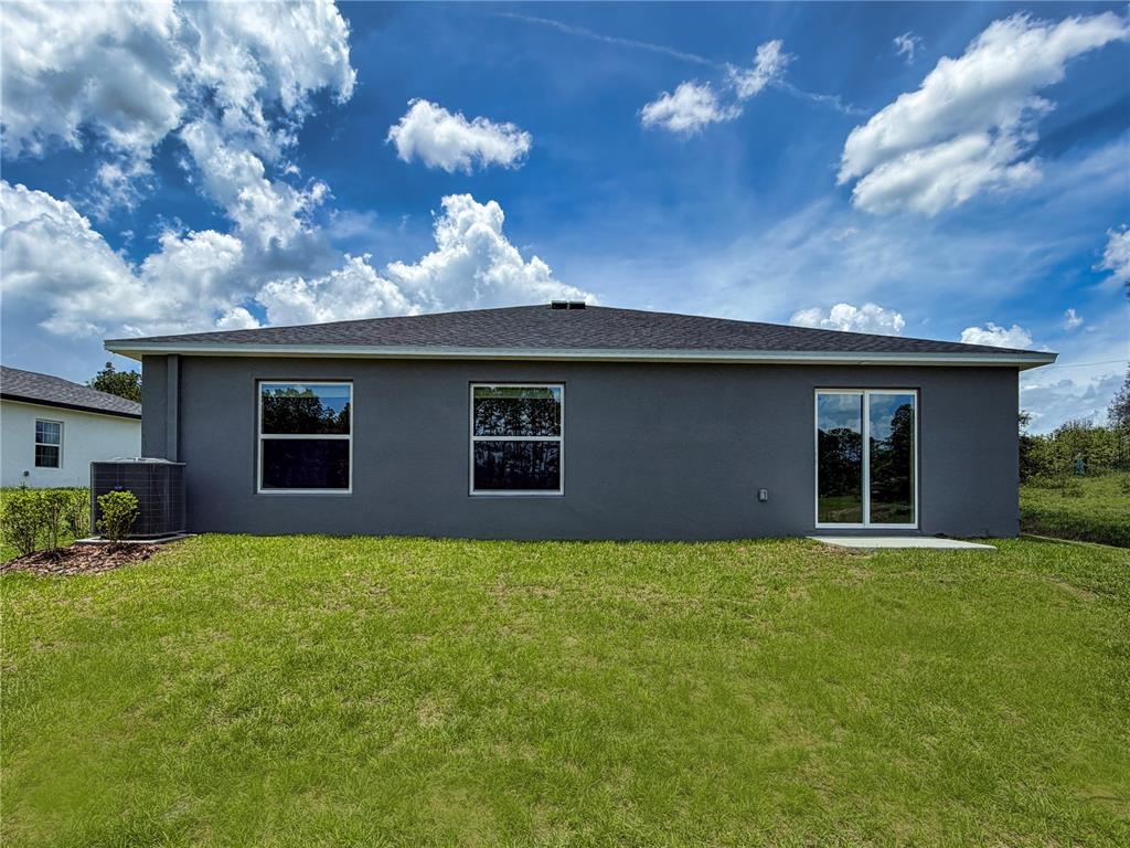 The rear exterior of a gray stucco house features two windows and a sliding glass door — 13079 SW 86TH COURT, OCALA, FL