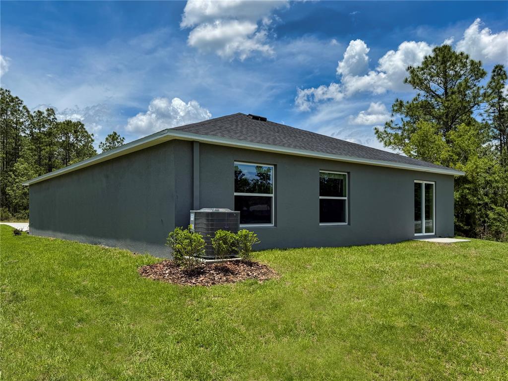 The rear exterior of a gray stucco house features two windows, a sliding door, and an AC unit — 13079 SW 86TH COURT, OCALA, FL