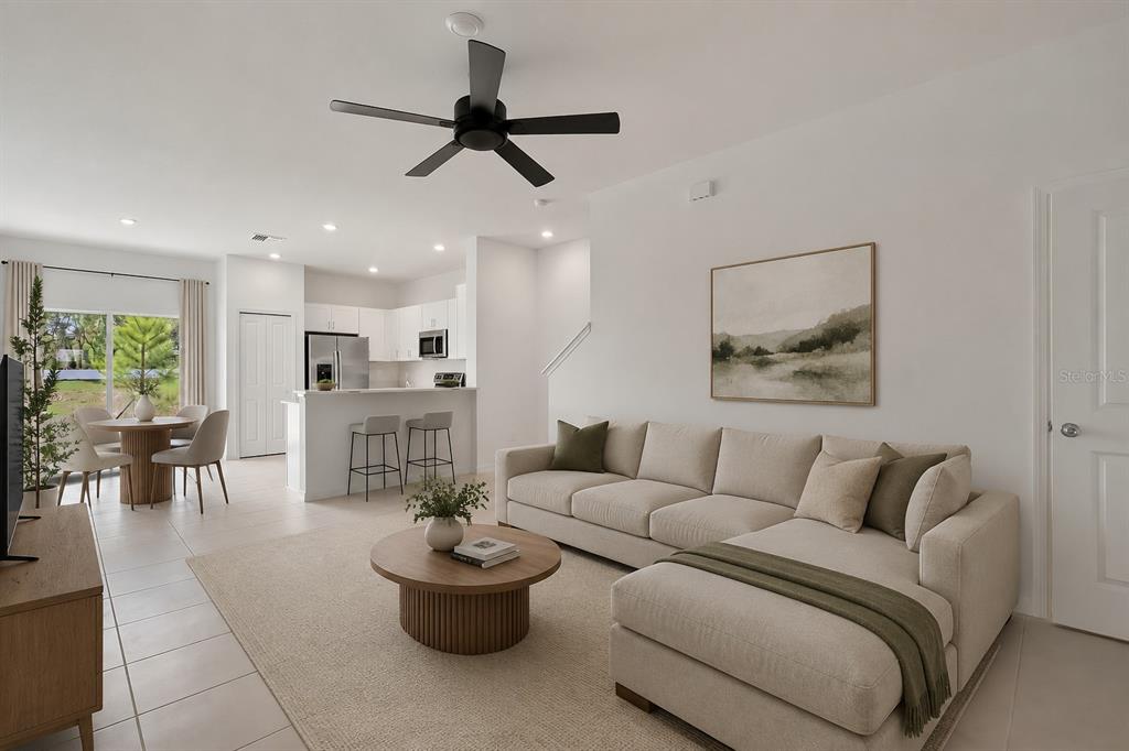 A modern living room and kitchen area with a sectional sofa, dining table, and ceiling fan — 36144 RISA MICHELE STREET, ZEPHYRHILLS, FL