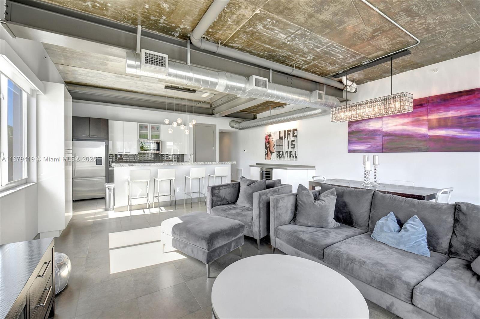 This open-concept living area features a kitchen, gray velvet furniture, and exposed industrial ductwork — 110 SE 2nd ST # 203, Delray Beach FL 33444, DELRAY BEACH, FL