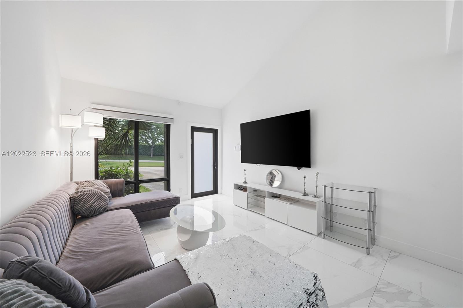 A modern living room features a grey sectional sofa, white tile floors, and a wall-mounted television — 455 NE 210th Ter, Miami FL 33179, MIAMI, FL